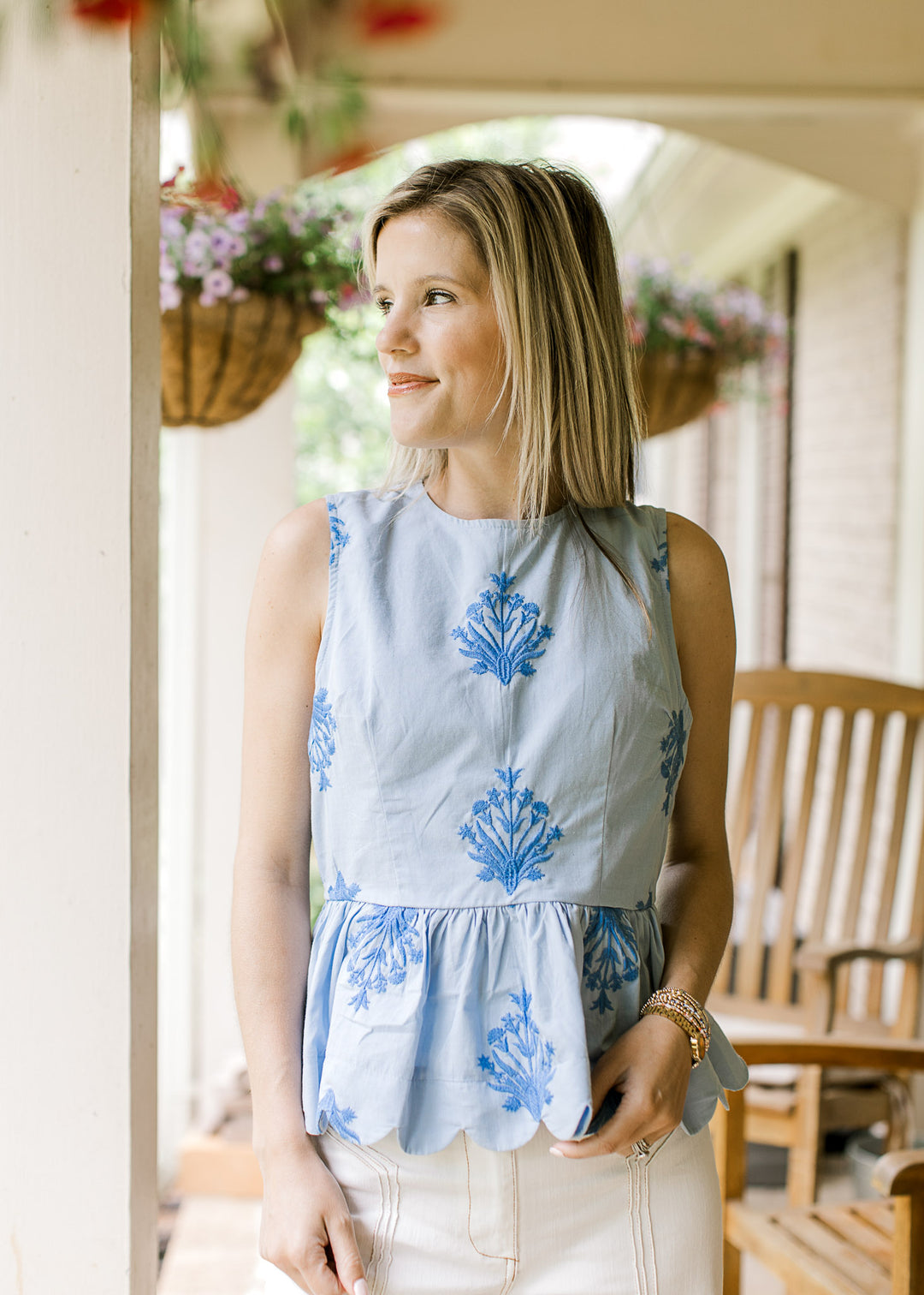 Model wearing a sleeveless baby blue top with embroidered deep blue floral and scalloped hem.
