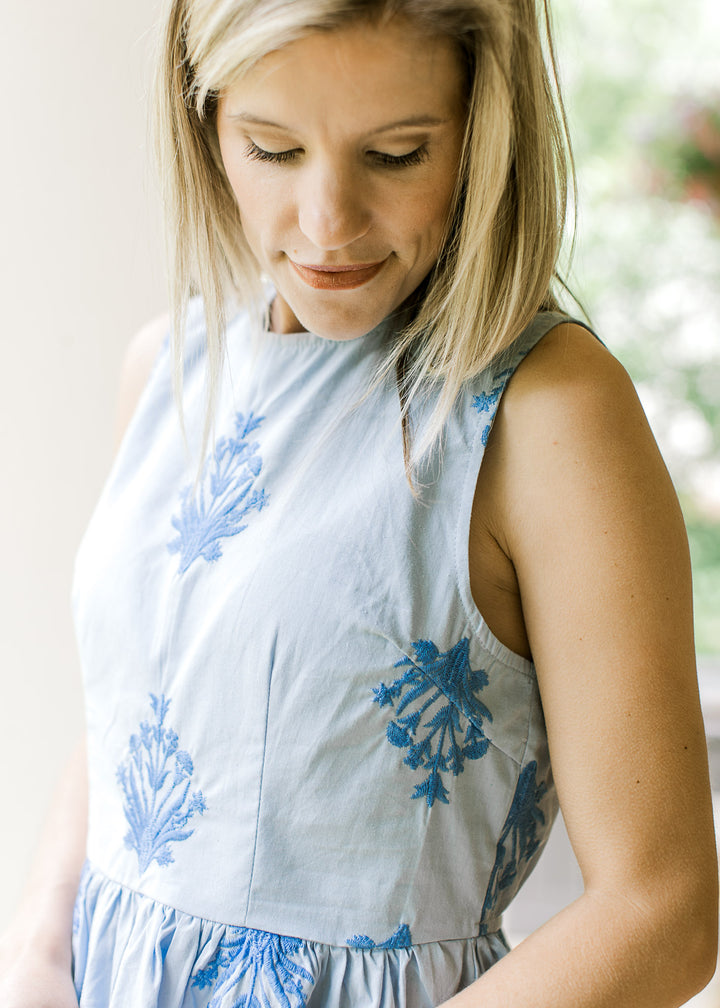 Close up of deep blue embroidered floral on a pale blue top with sleeveless fit and round neck.
