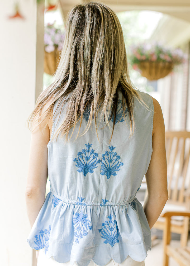 Back view of Model wearing a sleeveless baby blue top with deep blue floral and elastic waist.
