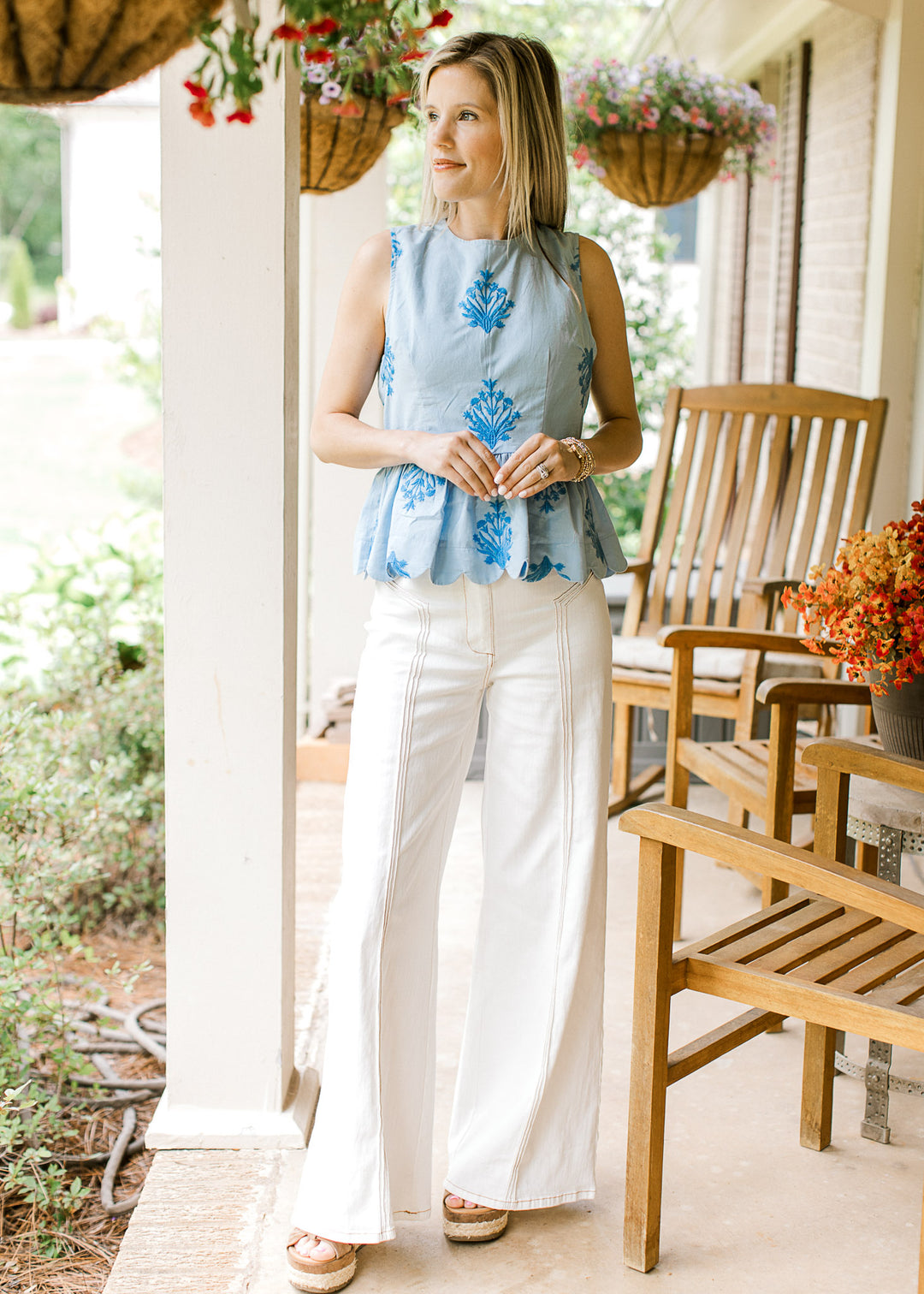 Model wearing white pants, heels and a baby blue top with embroidered deep blue floral. 

