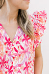 Close up of bold pink, orange and red flowers on a white top with ruffle short sleeves and a v-neck.