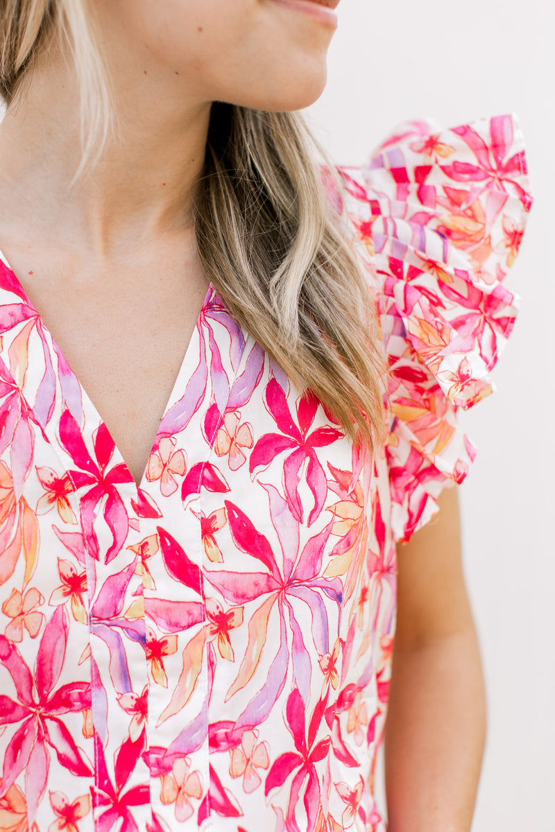 Close up of bold pink, orange and red flowers on a white top with ruffle short sleeves and a v-neck.