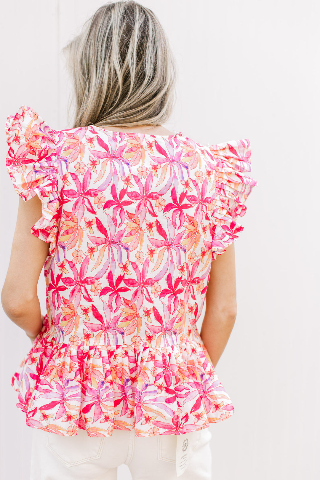 Back view of Model wearing a bold floral v-neck top with ruffle short sleeves and pleating detail.
