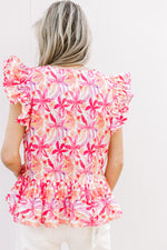 Back view of Model wearing a bold floral v-neck top with ruffle short sleeves and pleating detail.
