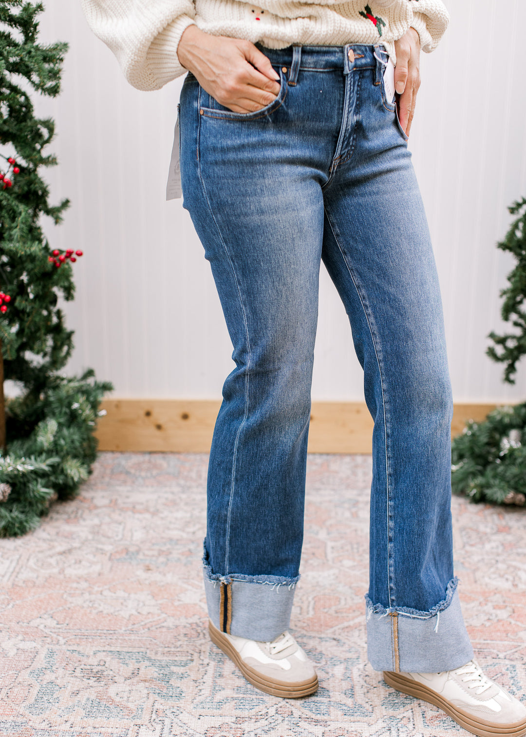  Front angled view of Risen high-rise flare jeans with faded blue wash, wide raw-edge cuffs and white sneakers.