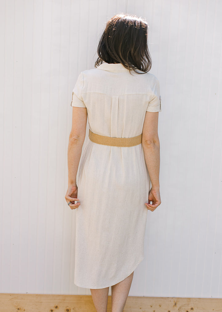 Back view of Model wearing a sandy linen dress with a collar, short sleeves with clasp and belt.