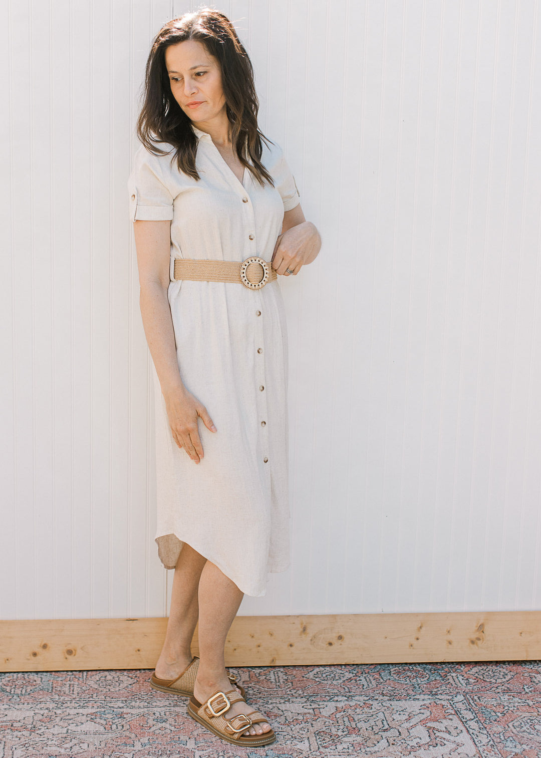 Side view of Model wearing a sandy linen dress with button front, collar, short sleeves and belt.