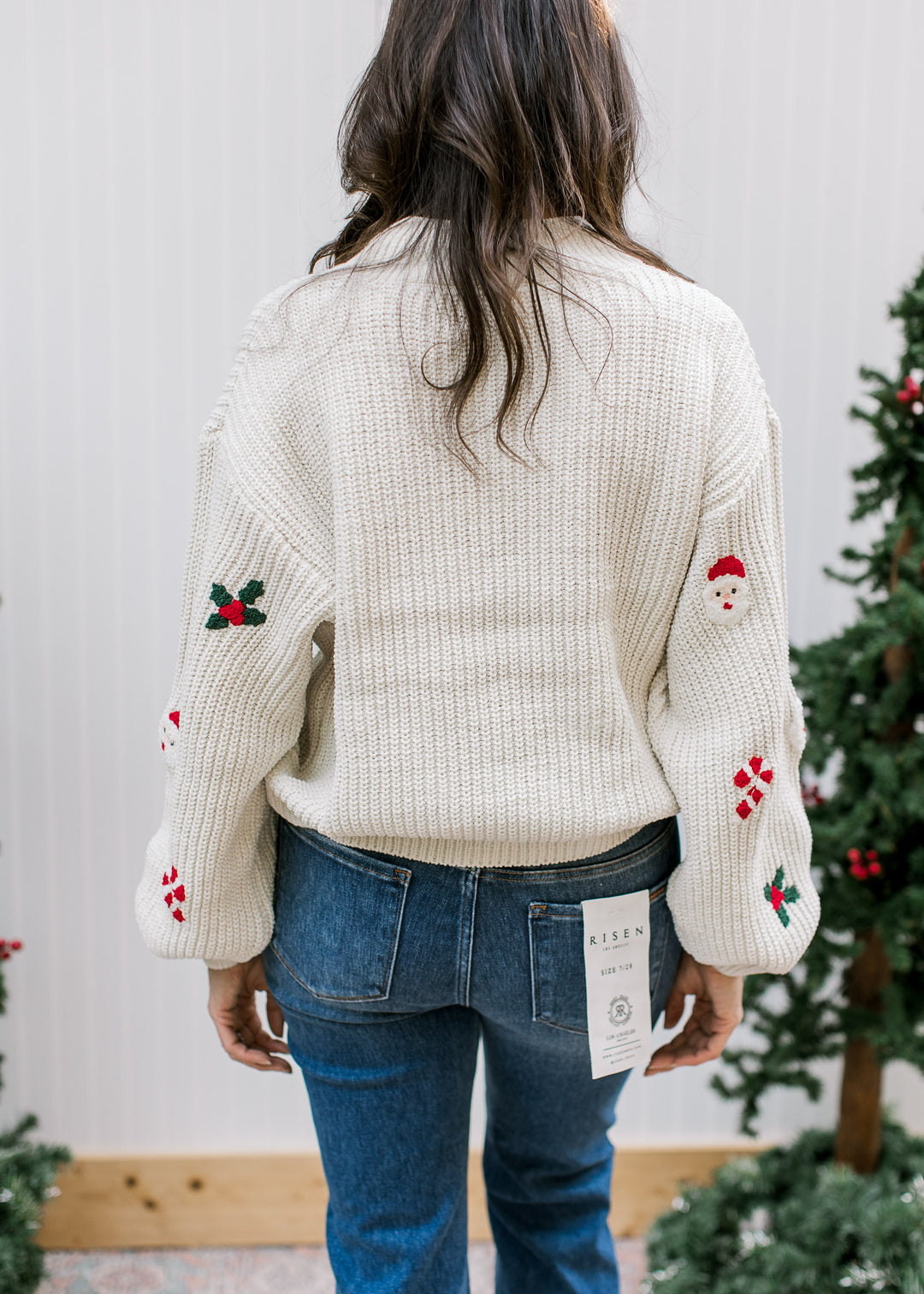 Back view of cream Santa sweater showing plain textured knit back, ribbed hem and festive motifs on long sleeves.
