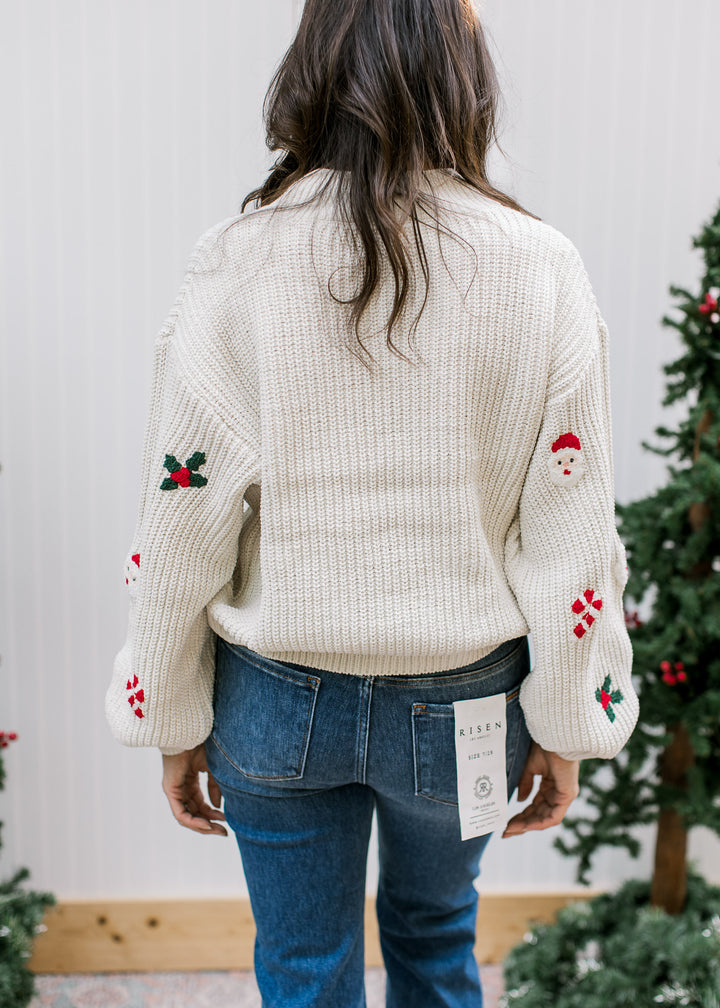 Back view of cream Santa sweater showing plain textured knit back, ribbed hem and festive motifs on long sleeves.