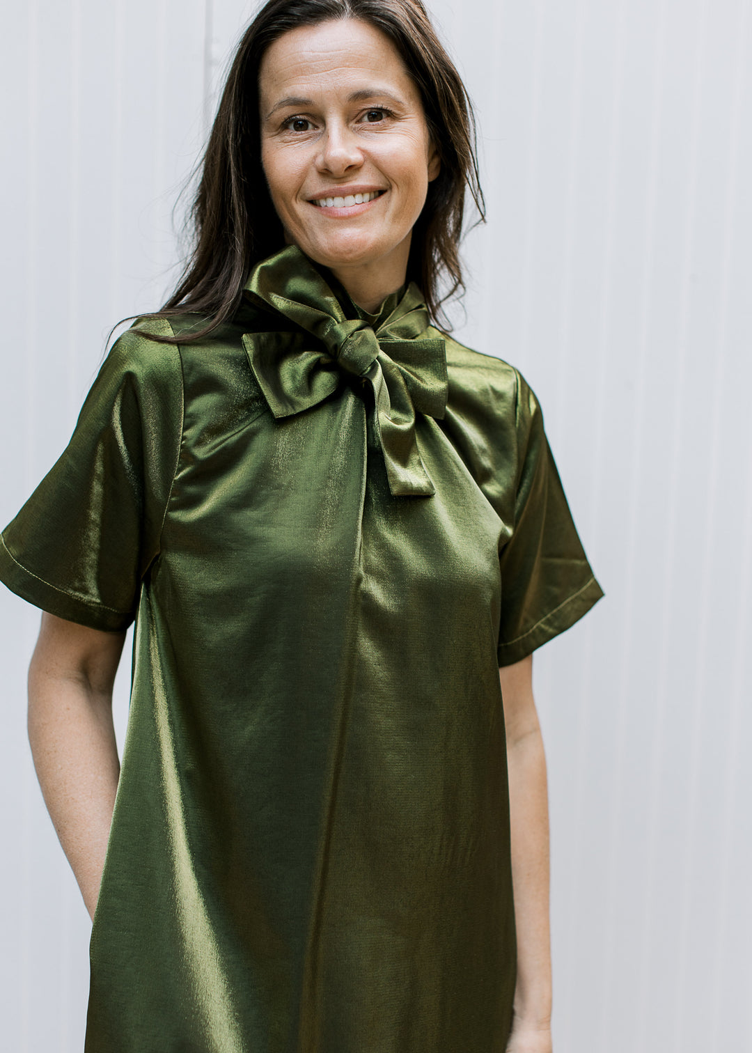 Close-up of silken olive dress with large front neck bow, gathered bodice, short sleeves and shimmering finish.