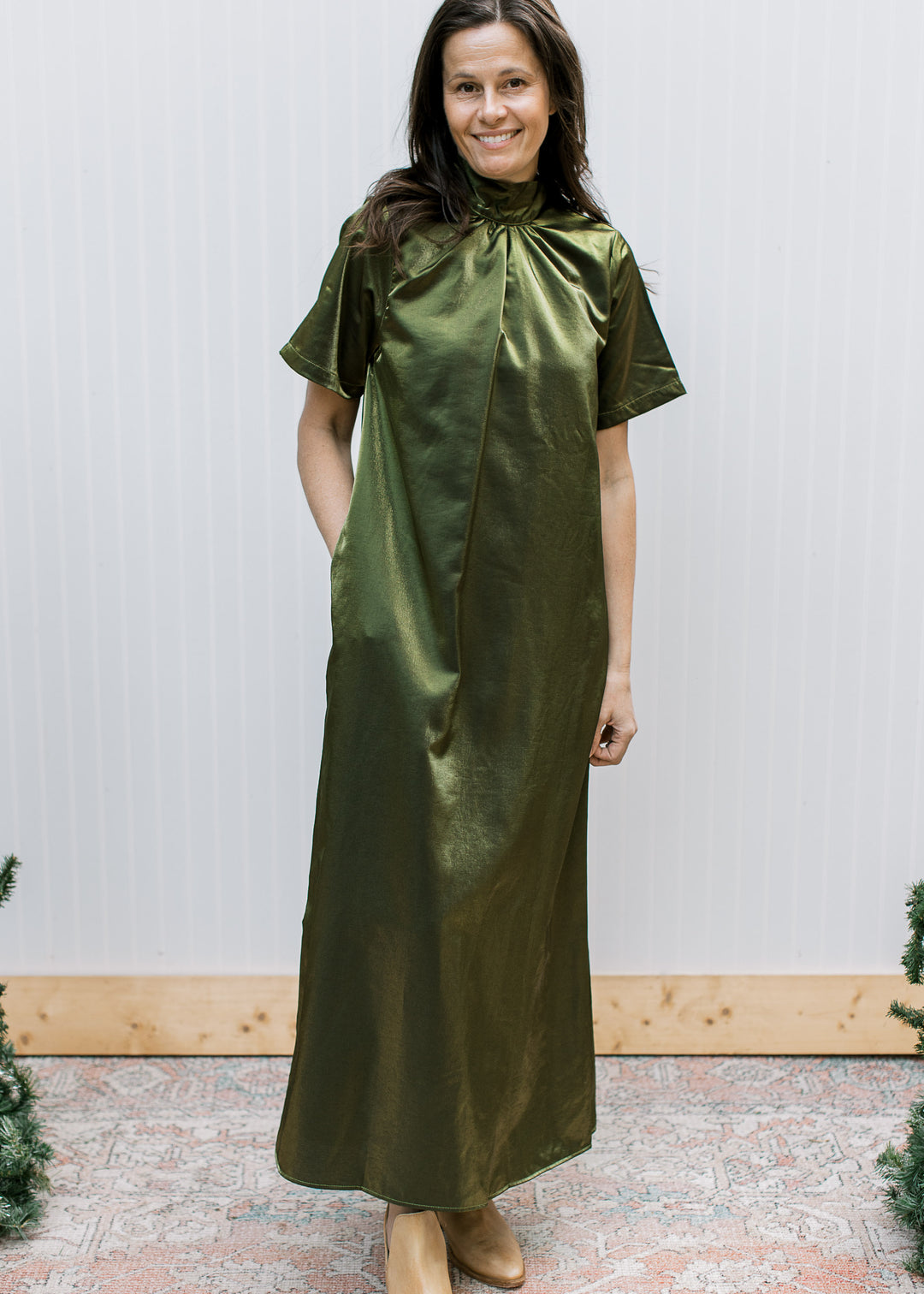Front view of shimmery olive maxi dress with gathered mock neckline, short sleeves and hand in a side pocket.