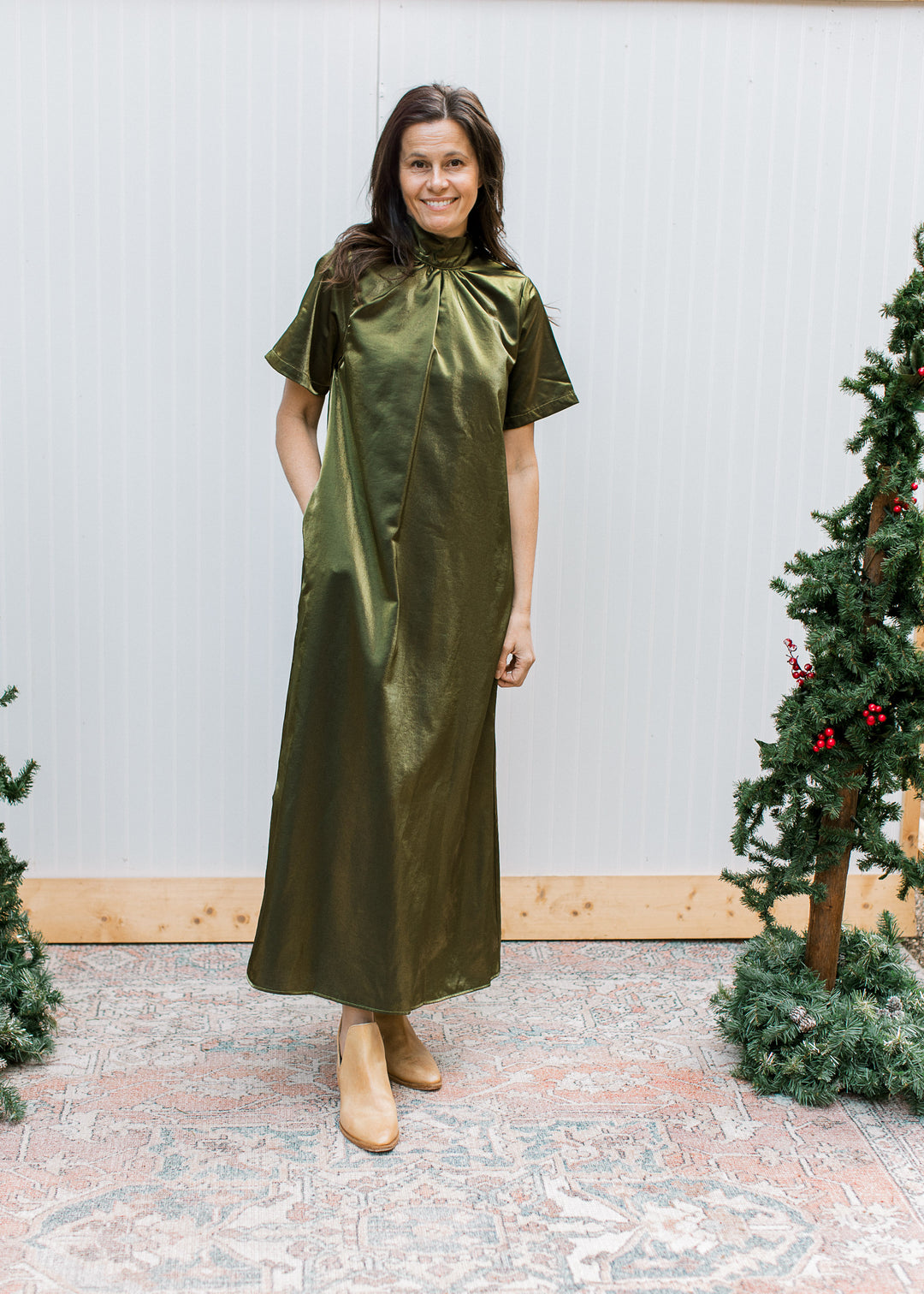 Full-length olive maxi dress with mock neckline and short sleeves, styled with tan ankle boots beside Christmas trees.