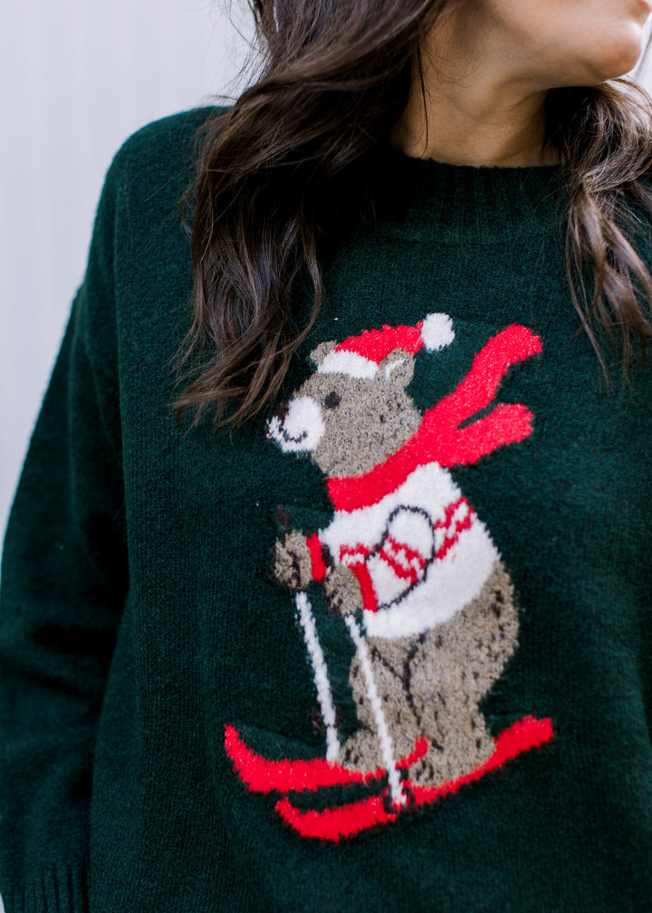 Close-up of hunter green sweater showing a skiing bear in a Santa hat, red scarf and white patterned sweater.