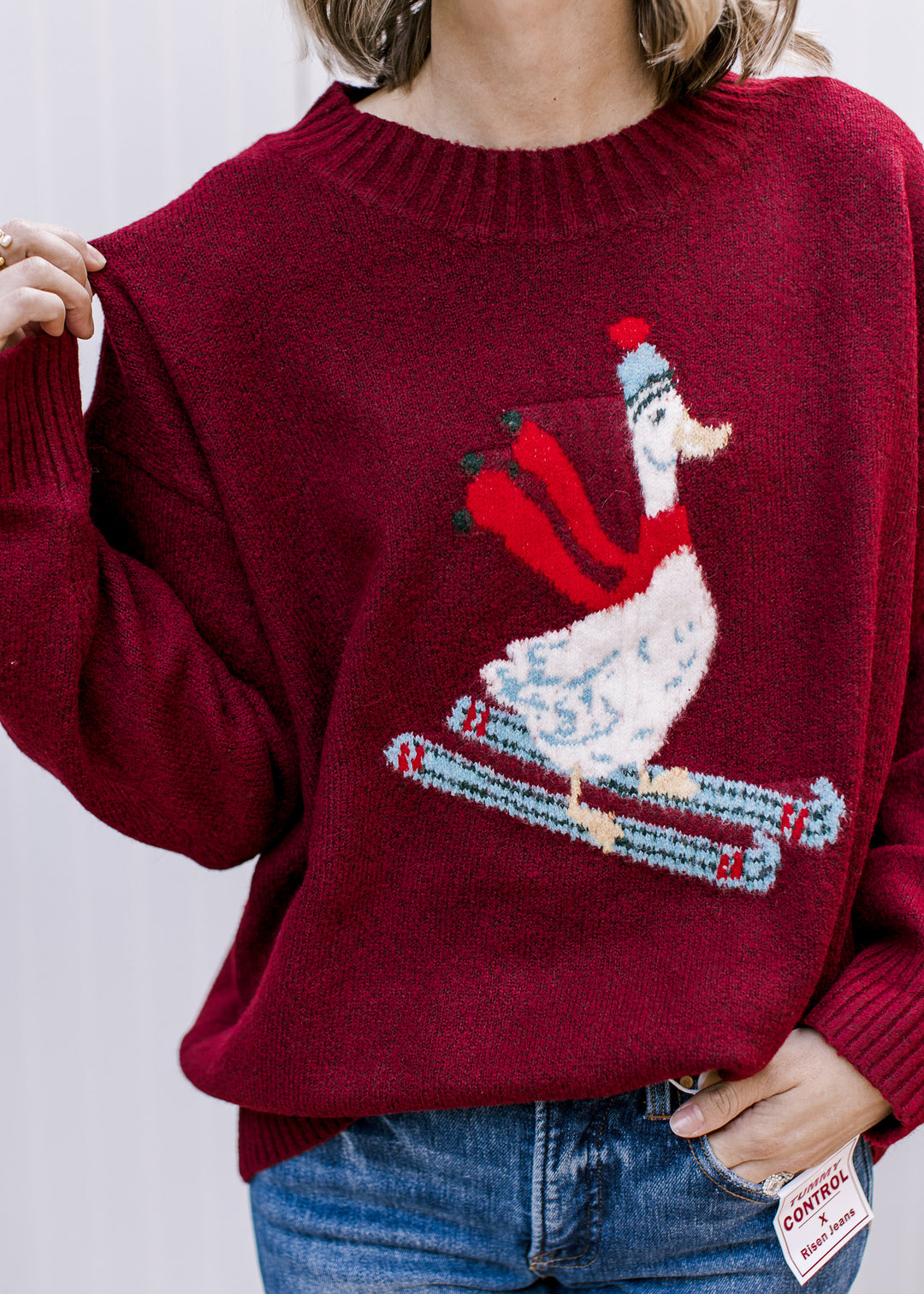 Close-up of burgundy sweater showing white skiing goose in a striped hat and red scarf, with blue patterned skis.