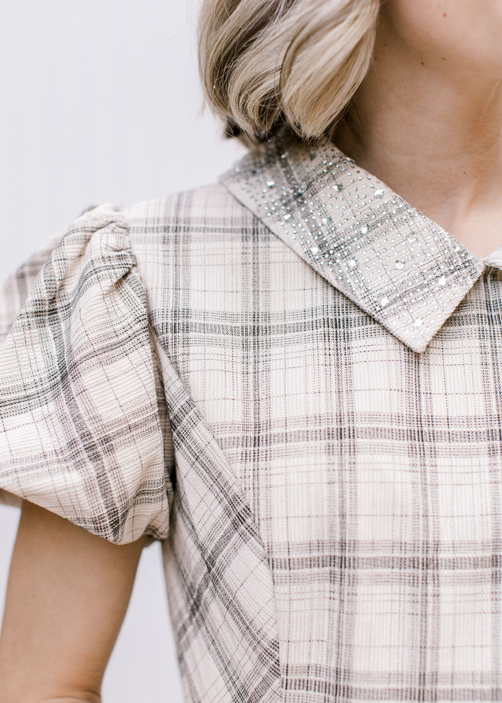 Close-up of taupe and black plaid top showing jeweled pointed collar, gathered shoulder and short bubble sleeve.