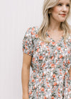 Close up of v-neck, short sleeves with elastic and elastic waist band on a white midi with tulips.