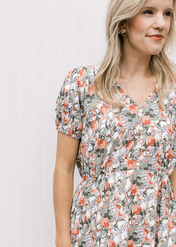 Close up of v-neck, short sleeves with elastic and elastic waist band on a white midi with tulips.