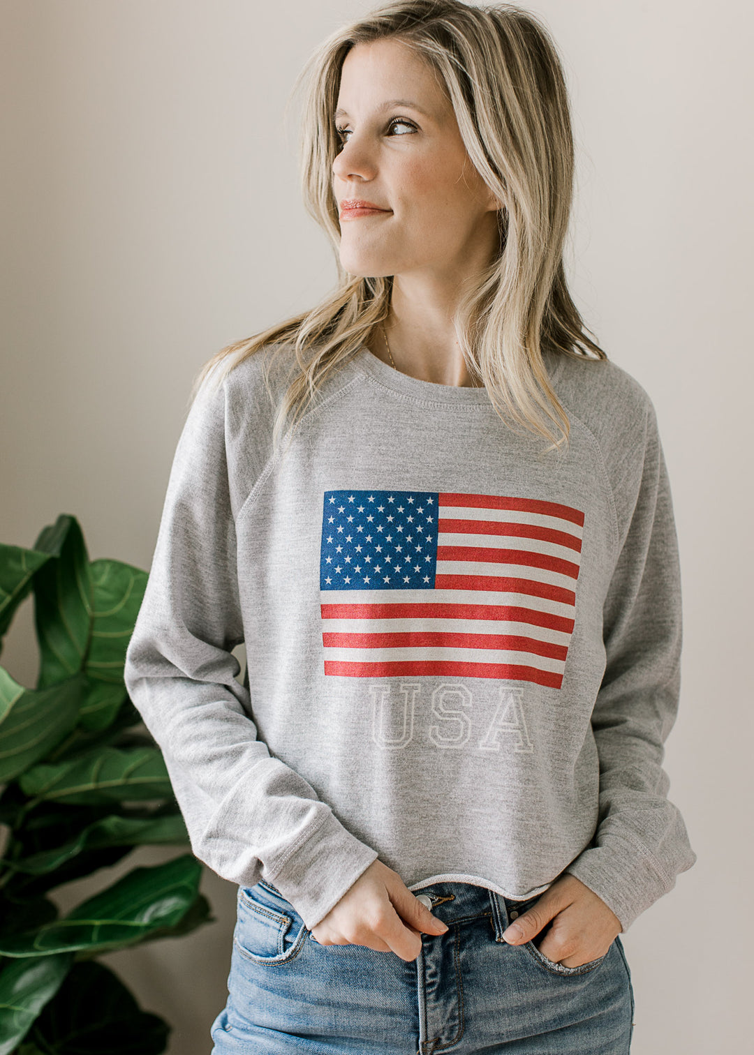 Model wearing a long sleeve gray top with USA flag and lettering, slightly cropped with rolled hem.