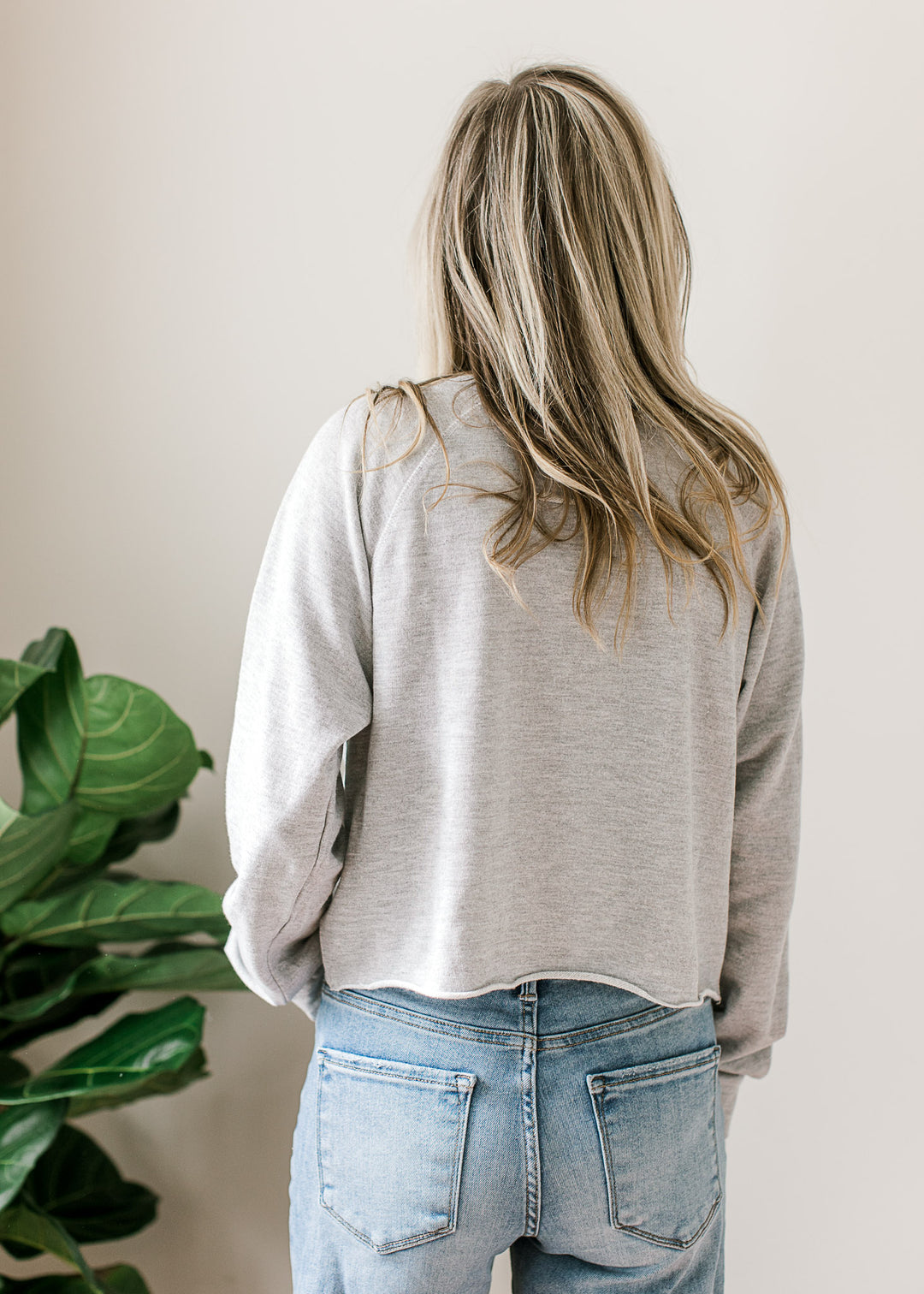 Back view of Model wearing a long sleeve gray top with USA flag and lettering and rolled hem. 