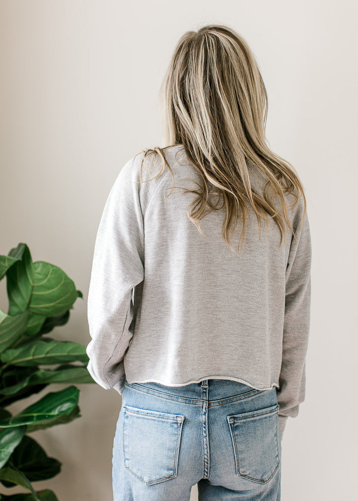 Back view of Model wearing a long sleeve gray top with USA flag and lettering and rolled hem. 