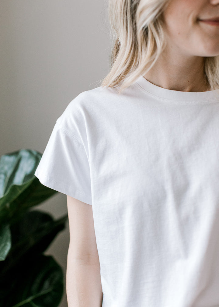 Model wearing a white top with a slightly cropped fit, short sleeves and a round neckline.