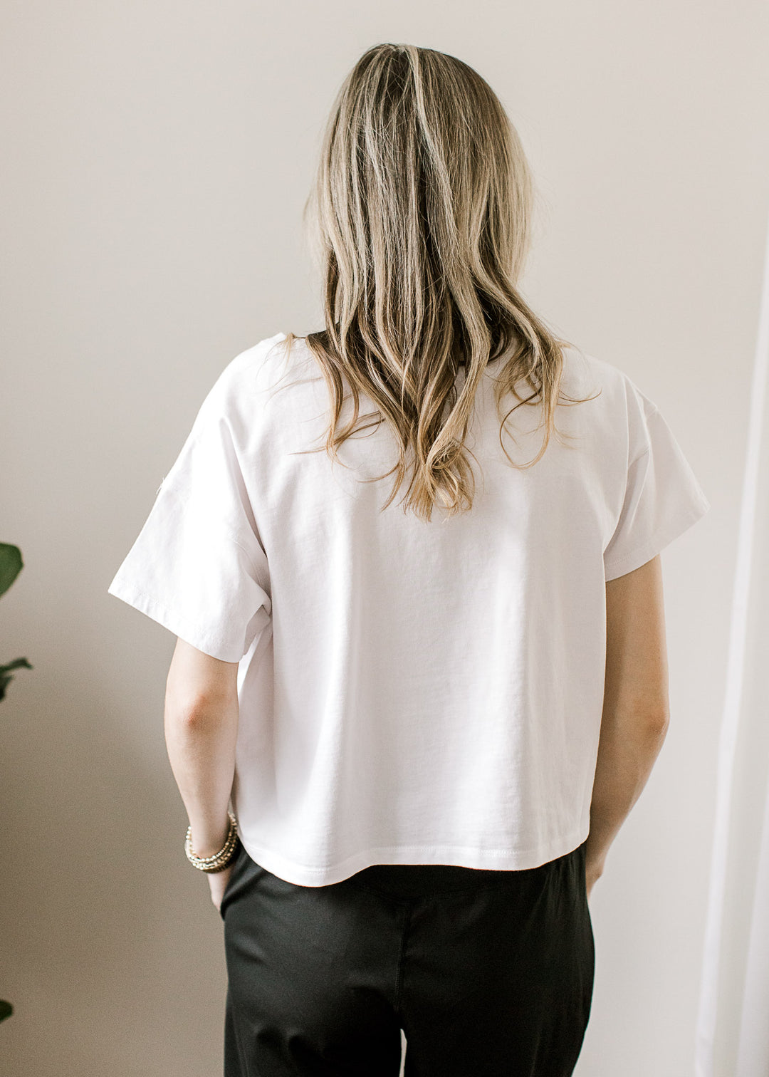 Back view of Model wearing a white top with a slightly cropped fit, short sleeves and a round neck. 