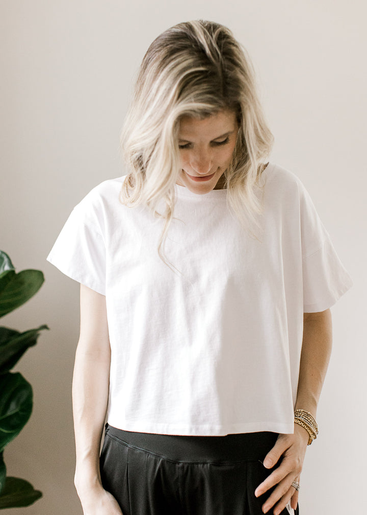 Model wearing black pants and a white top with a slightly cropped fit and short sleeves. 