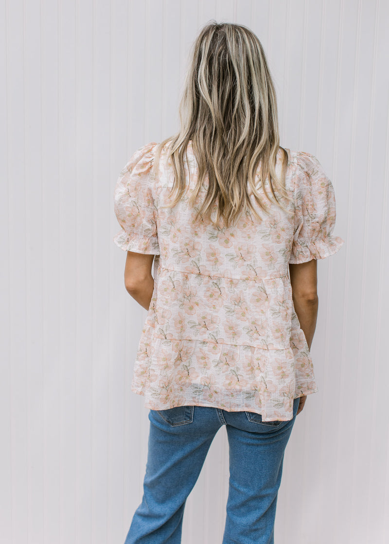 Back view of Model wearing a cream top with pink watercolor floral and sheer puff short sleeves