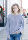 Model wearing a grayish blue sweatshirt with wide neck, long sleeves and exposed hem.