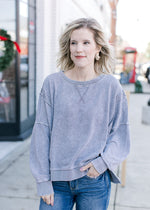 Model wearing a grayish blue sweatshirt with wide neck, long sleeves and exposed hem.