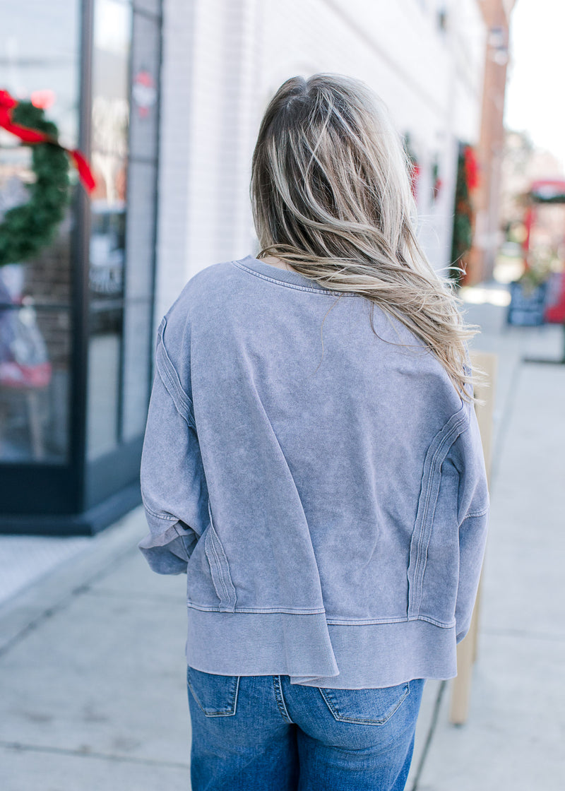 Back view of Model wearing a grayish blue sweatshirt with wide neck and long sleeves.