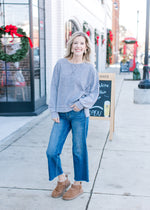 Model wearing jeans, booties and a grayish blue sweatshirt with long sleeves. 