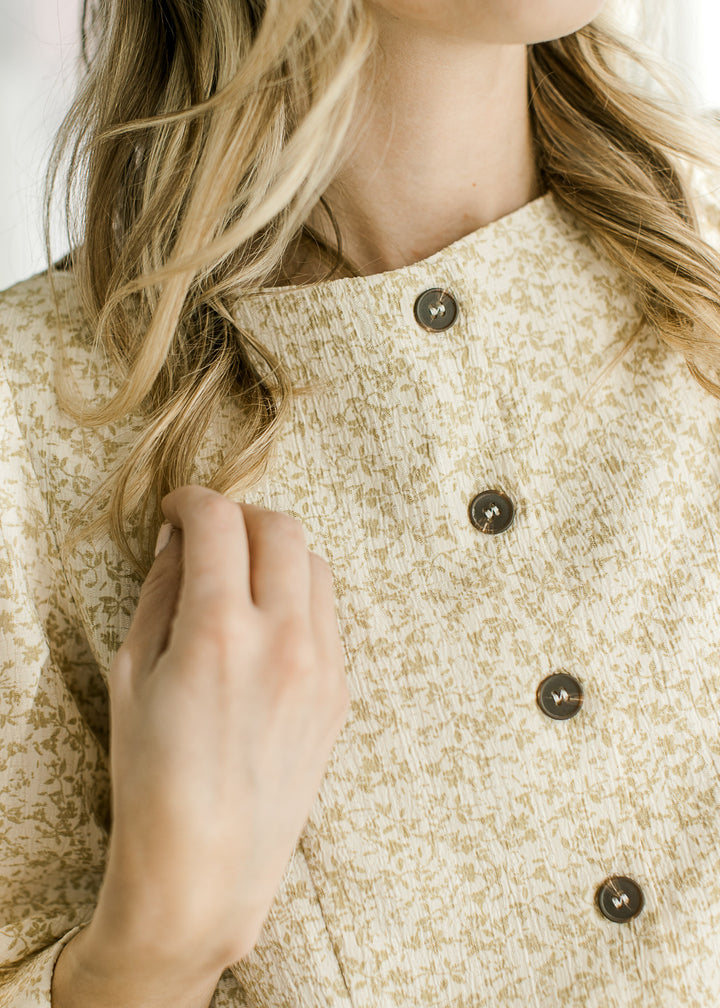 Close up of boatneck and buttons on a cream top with taupe ditsy floral and 3/4 bubble sleeves. 
