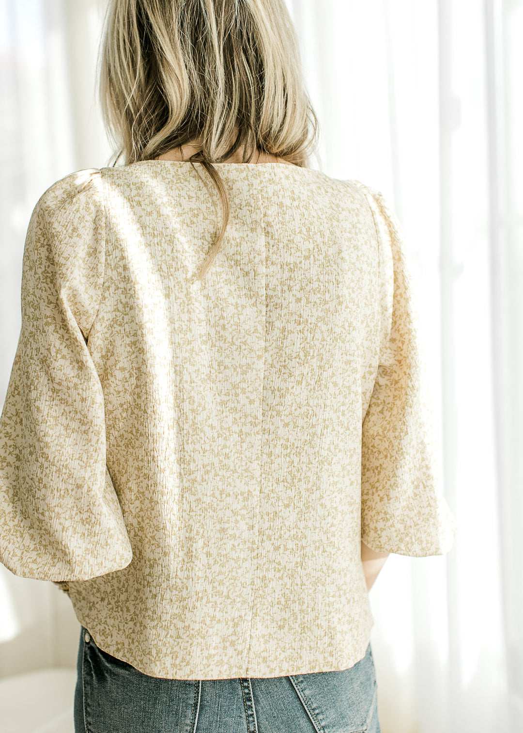 Back view of Model wearing a cream top with taupe ditsy floral, boatneck and 3/4 bubble sleeves.