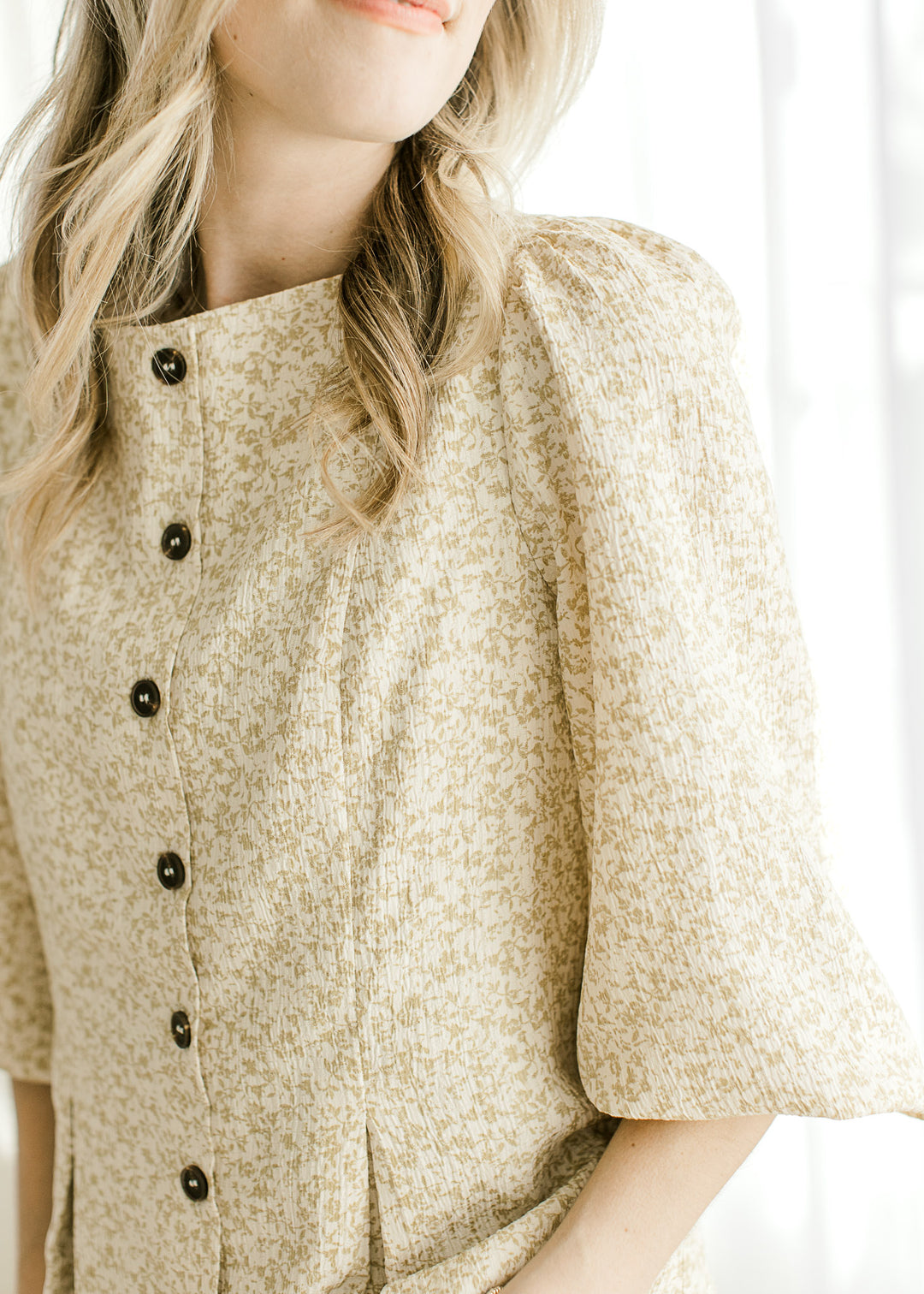 Close up of 3/4 bubble sleeves with pleated shoulders on a cream top with taupe floral. 