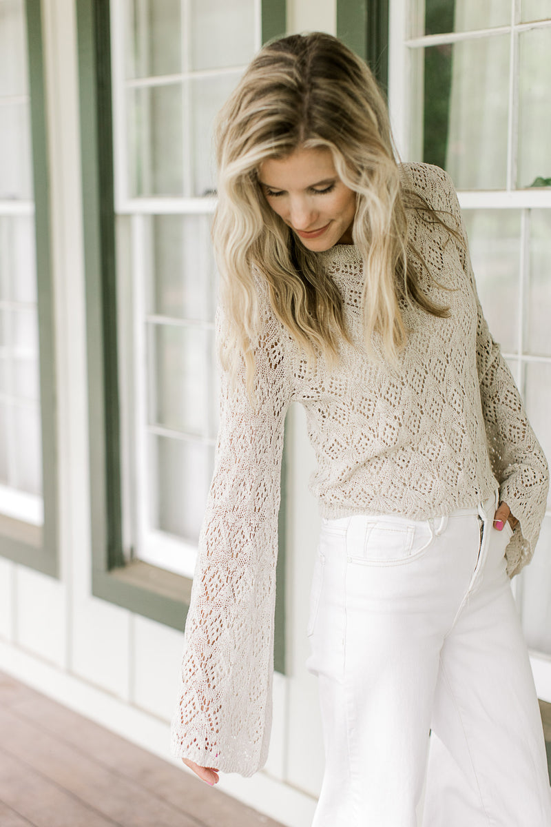 Model wearing white pants with a cream sweater with scallop detail at the neck, cuff and hem.