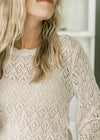 Close up of open knit detail on a cream sweater with scallop detail at neck, cuff and hem.