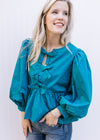 Model wearing a teal top with bow details down front, bubble long sleeves and pleated shoulders.