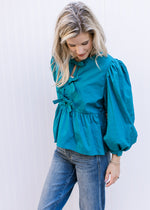 Model wearing jeans and a teal top with bow details, bubble long sleeves and pleated shoulders.