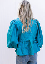 Back view of Model wearing a teal top with bubble long sleeves and pleated shoulders.