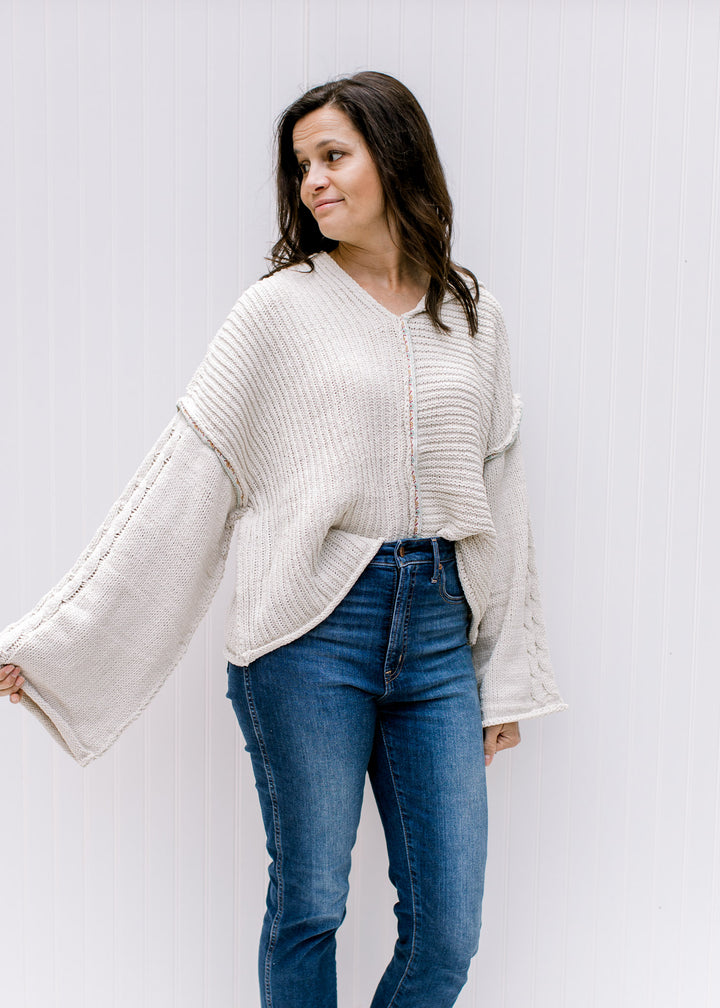 Model wearing a cream cable knit sweater with kimono long sleeves and a hood. 