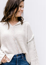 Model wearing a cream cable knit sweater with kimono long sleeves, a hood and exposed hem.