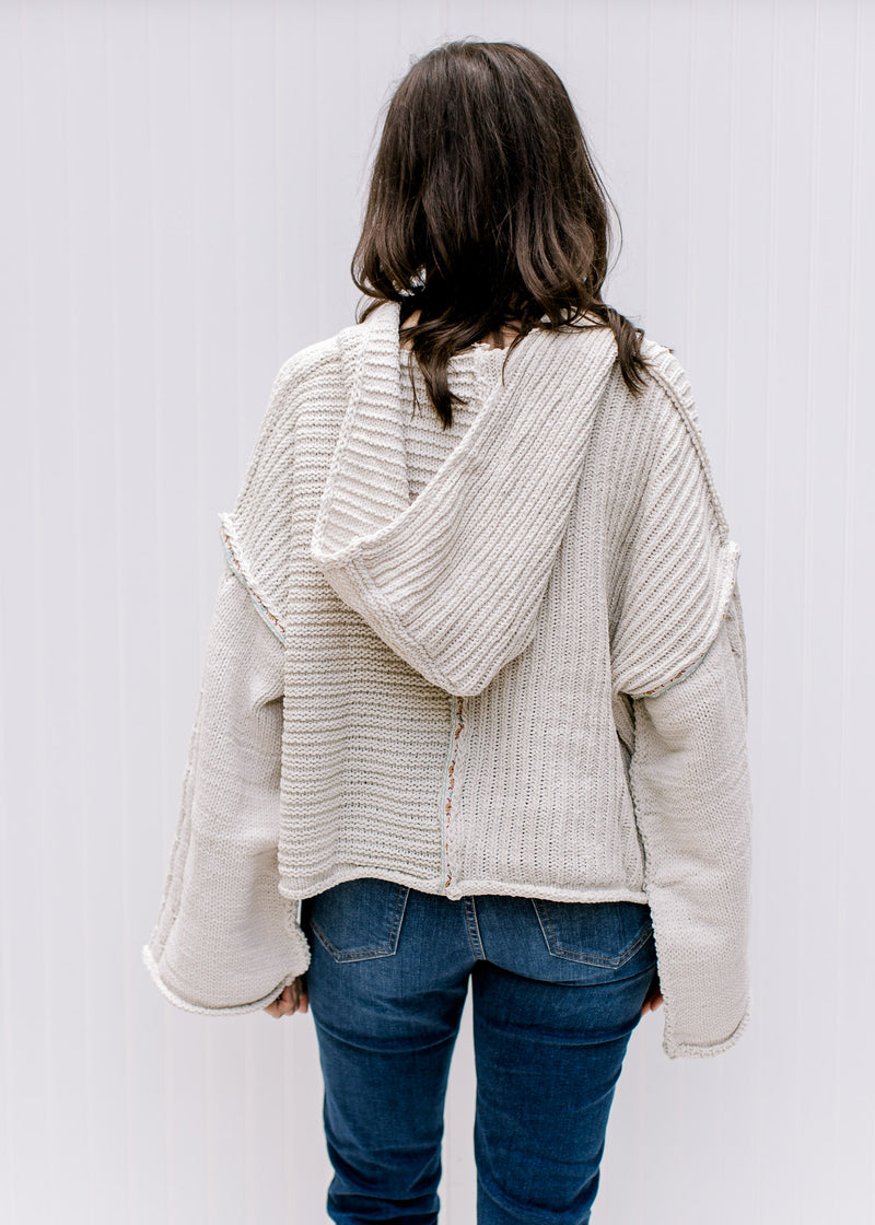 Back view of Model wearing a cream cable knit sweater with kimono long sleeves and a hood. 