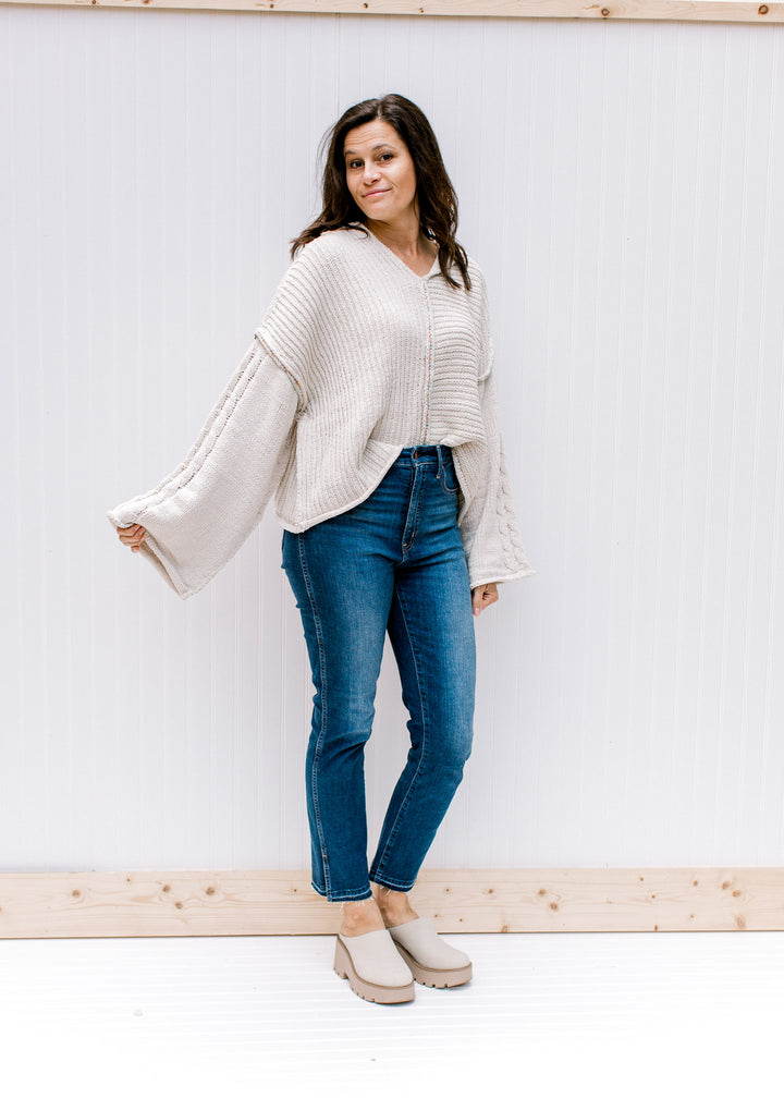 Model wearing jeans, mules and a cream cable knit sweater with kimono long sleeves and a hood. 