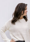 Close up of Model wearing a cream knit hoodie with a slightly cropped hem and long sleeves. 