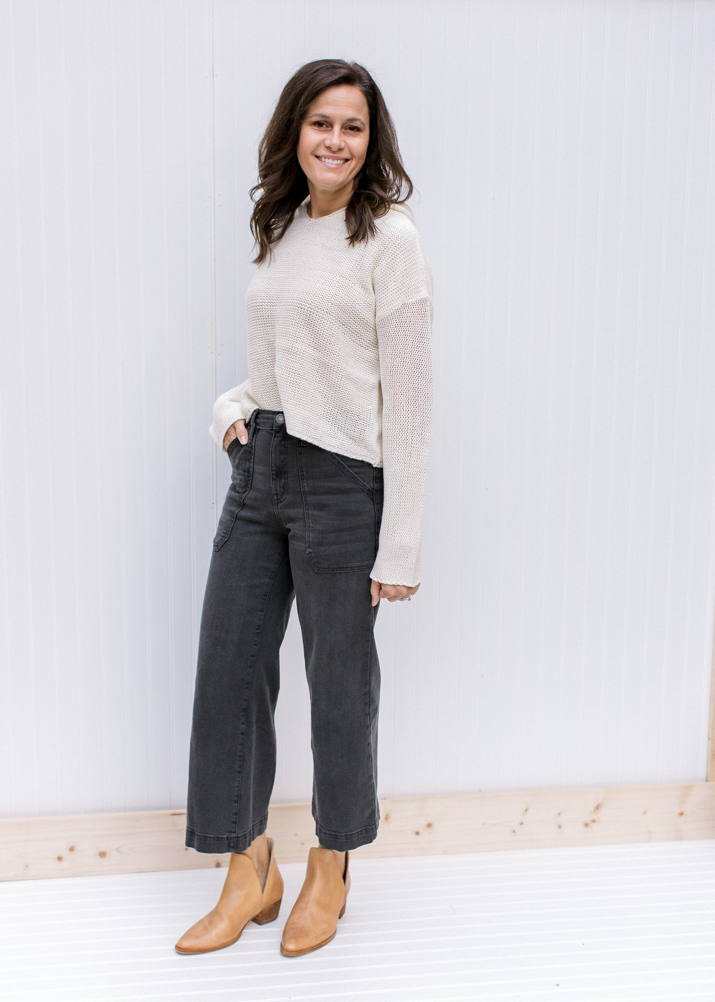 Model wearing jeans, booties and a cream knit hoodie with a slightly cropped hem and long sleeves. 