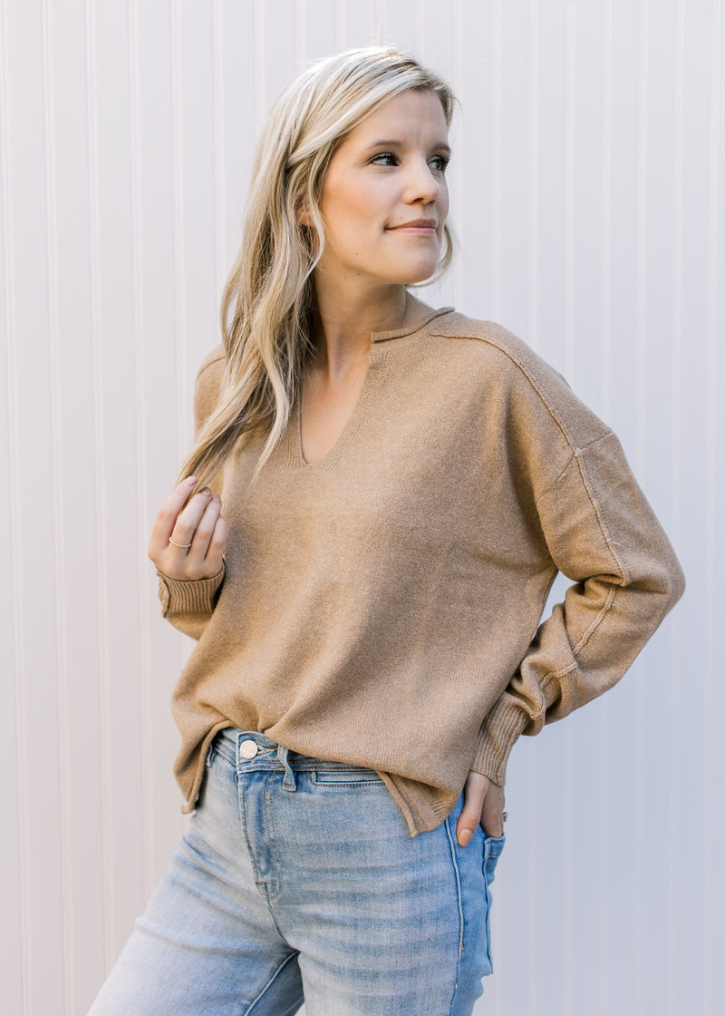 Model wearing a camel v-neck sweater with exposed hem, long sleeves and split sides. 