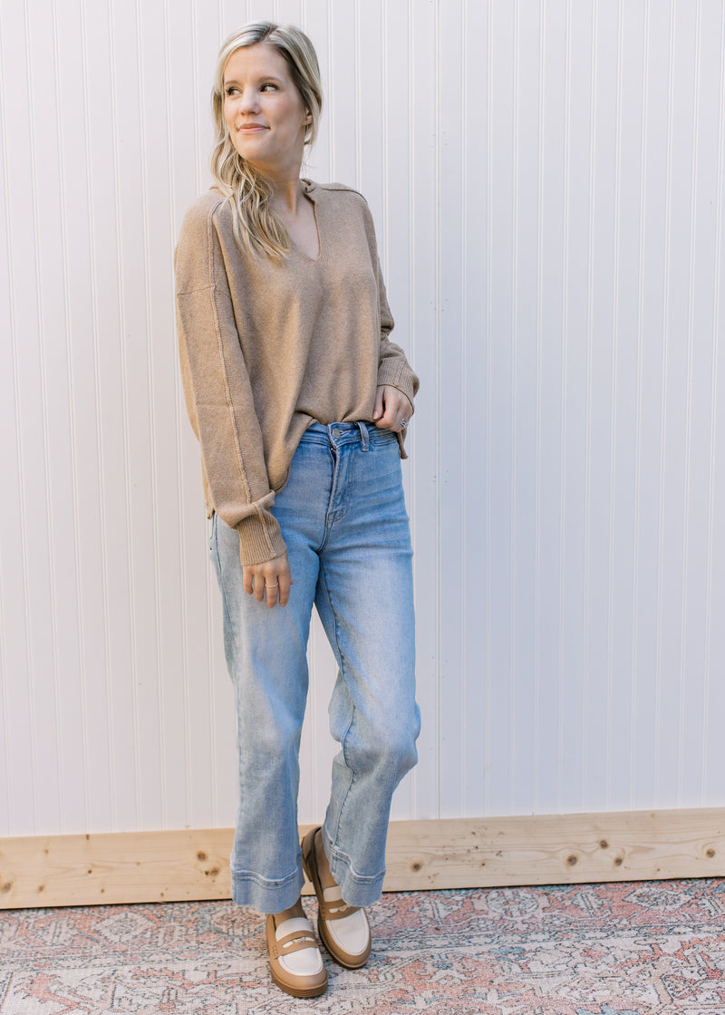 Model wearing jeans, loafers and a camel sweater with rolled hem, v-neck and long sleeves.