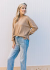 Model wearing jeans with a camel v-neck sweater with exposed hem, long sleeves and split sides. 