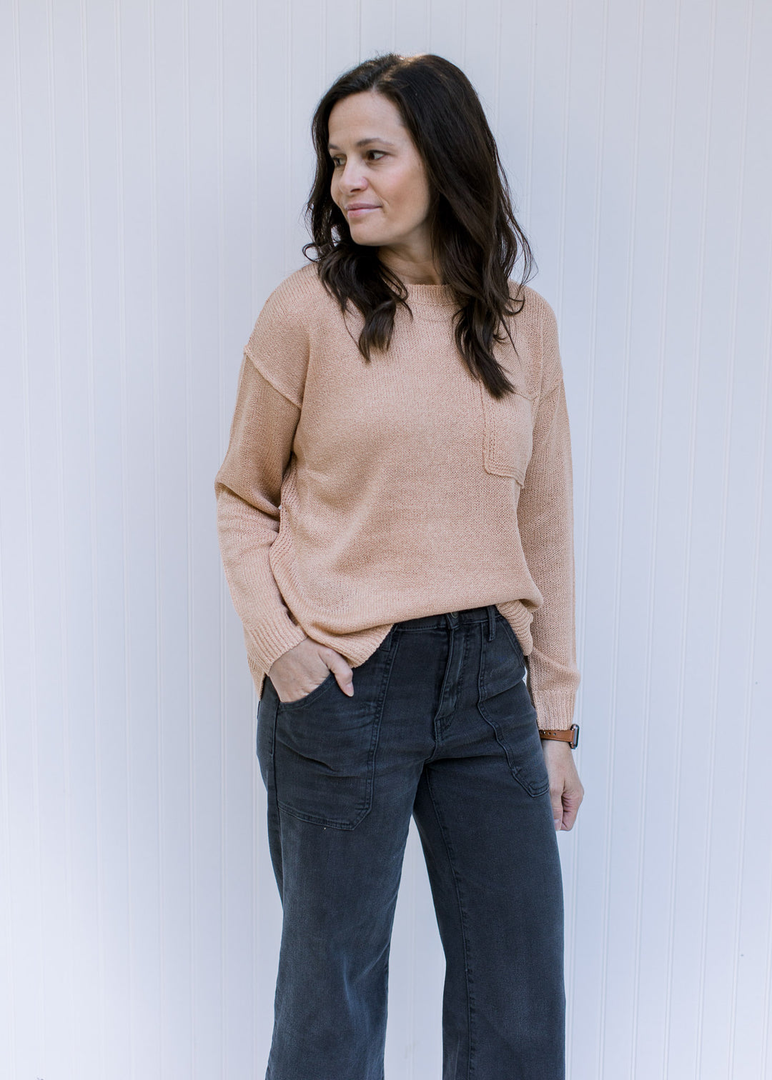 Model wearing an amber colored sweater with a patch pocket, exposed hem and long sleeves. 